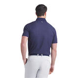 Man wearing a navy blue polo shirt and white pants on a light gray background