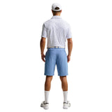 Man wearing a patterned polo shirt, blue shorts, and white cap on a light gray background